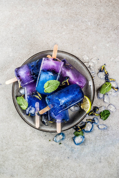 Naturally organic summer sweets, homemade blue and violet ice cream popsicles with butterfly pea flower tea, grey concrete background copy space - Foto, Bild