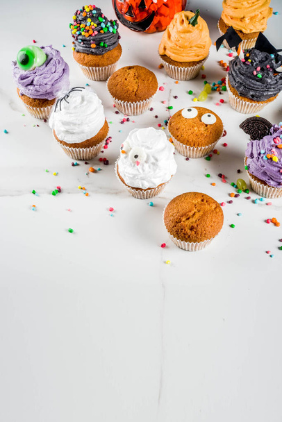 Funny children's treats for Halloween: variations of cupcakes, decorated in the form of different monsters, witches, pumpkins, ghosts. White marble background copy space for text, - Photo, Image