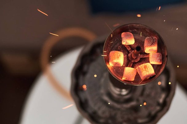 Close-up of shisha hookah with red hot coals. Sparks from breathe. Modern hookah with coconut charcoal and shisha smoke. - Fotó, kép
