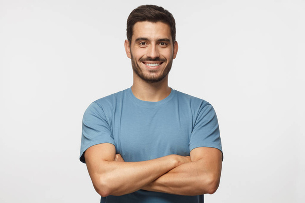 Portrait of smiling handsome man in blue t-shirt standing with crossed arms isolated on grey background - Фото, зображення