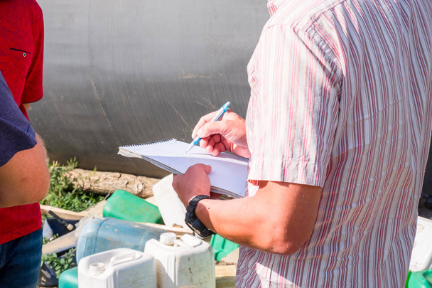 a man in a colored shirt with a notebook in his hands writes with a pen, discusses with another person in the field in the summer agronomist - Fotó, kép