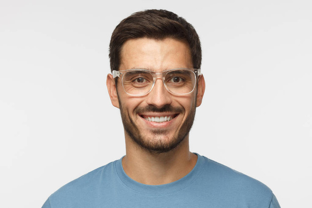 Smiling modern nice guy in blue t-shirt and trendy trasparent eyeglasses isolated on gray background - Фото, зображення