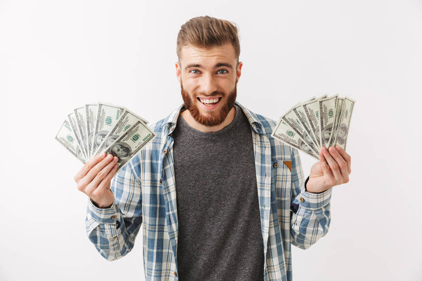 Portrait of a happy young bearded man standing isolated over white, showing money banknotes - Foto, Bild