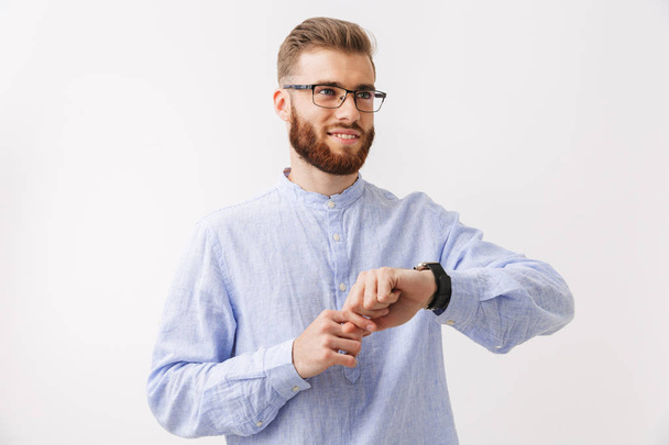 Portret van een lachende jonge bebaarde man boven wit, geïsoleerd staan smartwatch waarop zijn pols - Foto, afbeelding