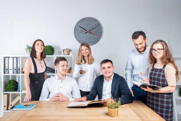 Thema is business en teamwork. Een groep van jonge Kaukasische mensen kantoorpersoneel een bijeenkomst, briefing, werken met papieren en documenten in een lichte bureaubureau rond een houten tafel. - Foto, afbeelding