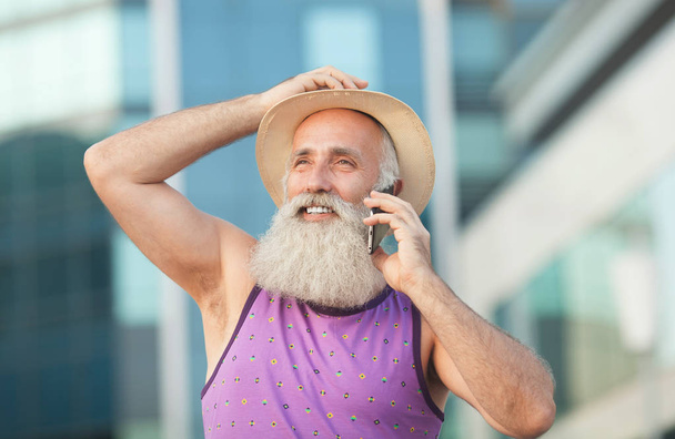 happy senior bearded tourist man smiling and giggling while using mobile phone - Фото, зображення