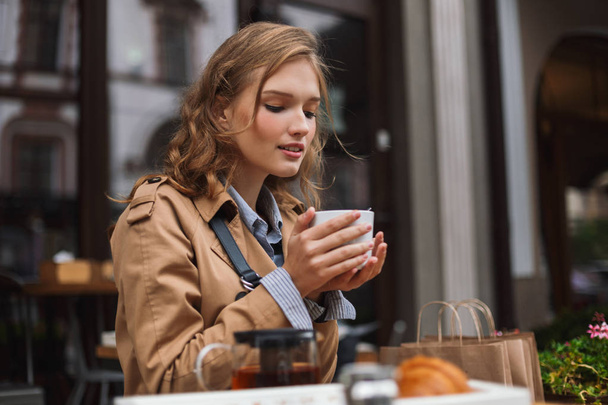 Gyönyörű lány álmodozva teázás időt szabadtéri teraszon hangulatos kávézó viharkabát - Fotó, kép