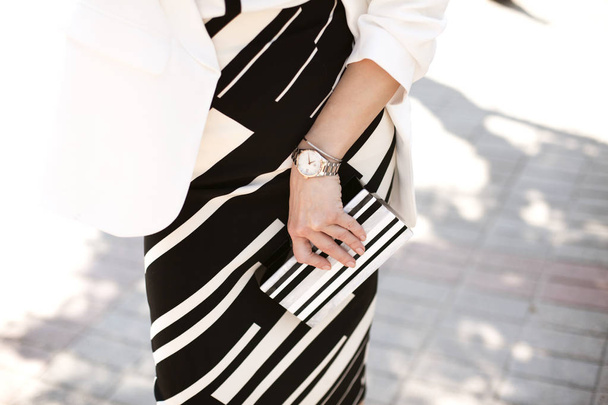 La chica camina por la ciudad en una elegante falda a rayas y con un embrague en blanco y negro, vista superior, detalles
 - Foto, Imagen