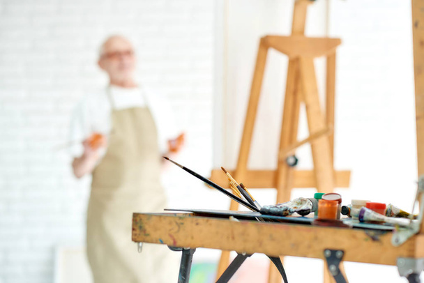 Drawing instruments and easel with male artist on blur background at studio. - Fotoğraf, Görsel