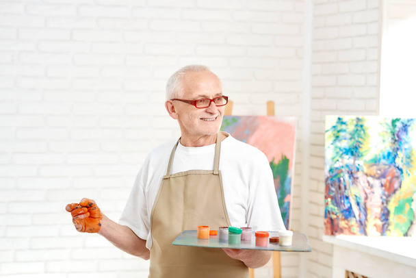 Senior male painter, standing with palette of colors in hand at studio. - Foto, Imagem