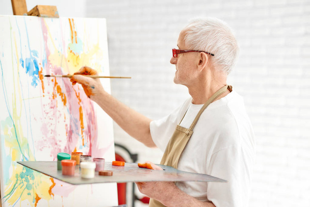 Senior talented painter while painting his masterpiece at studio. - Fotó, kép