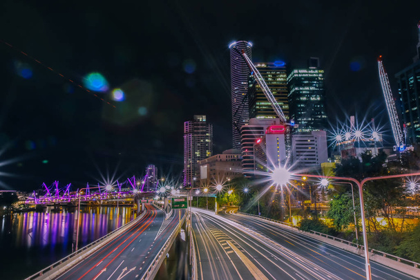 Majestueuze uitzicht op fel verlichte weg en stad o Brisbane in de buurt van rivier bij donkere nacht in Australië - Foto, afbeelding