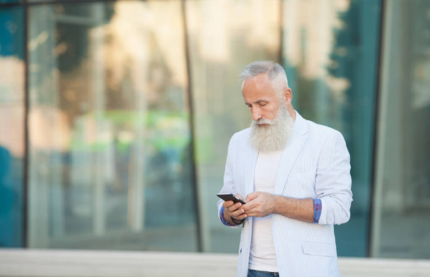 Trendy senior man using smartphone in downtown center outdoor - Mature fashion male having fun with new trends technology - Tech and joyful elderly lifestyle concept - Zdjęcie, obraz