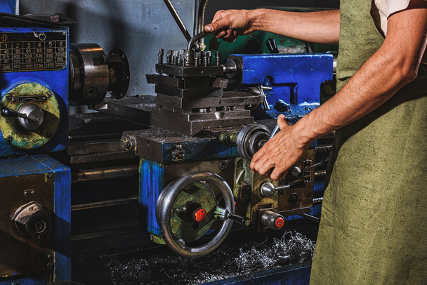 Teilansicht eines männlichen Fertigungsarbeiters in Schutzschürze mit Werkzeugmaschine in der Fabrik - Foto, Bild