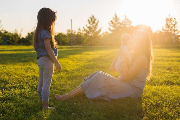 Young woman with son and daughter on the meadow on a sunny day. Happy family on summer sunset. Mother with baby. - Foto, Bild