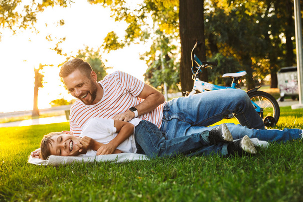 Excited father and his son having fun together at the green park, laying on a blanket - Foto, Imagem