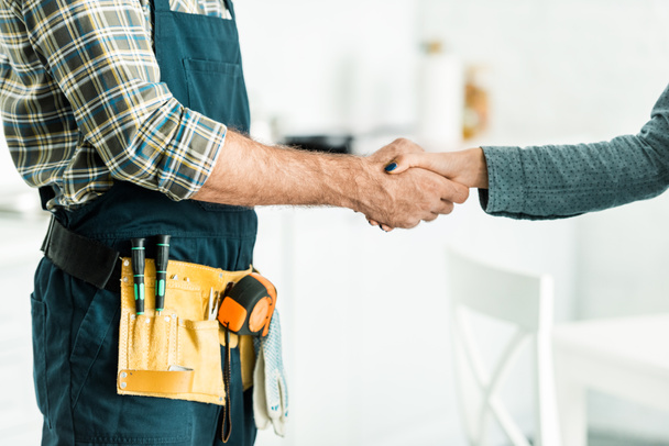 cropped image of plumber and client shaking hands in kitchen - Photo, Image