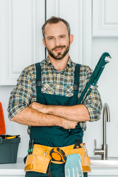 handsome plumber holding monkey wrench and looking at camera in kitchen - Photo, image