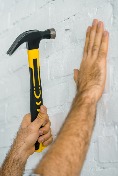 обрезанное изображение ремонтника, забивающего гвоздь в белую стену
 - Фото, изображение