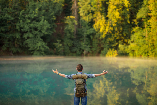 young man wearing backpack is praying in front of the river. meditation concept. back view photo - Photo, image