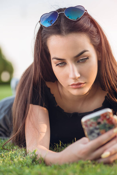 Sad teenage girl is texting lying on the grass - Fotó, kép