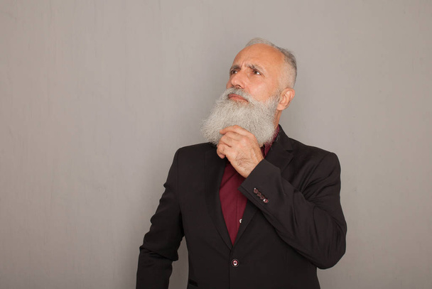 Bearded senior man thinking on grey background. - Photo, Image