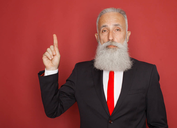 Excited old bearded businessman having an idea and pointing finger up at copy space isolated over red background - Fotografie, Obrázek