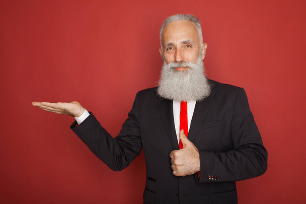 Bearded senior man smiling and holding something imaginary in one hand on red background - Photo, image