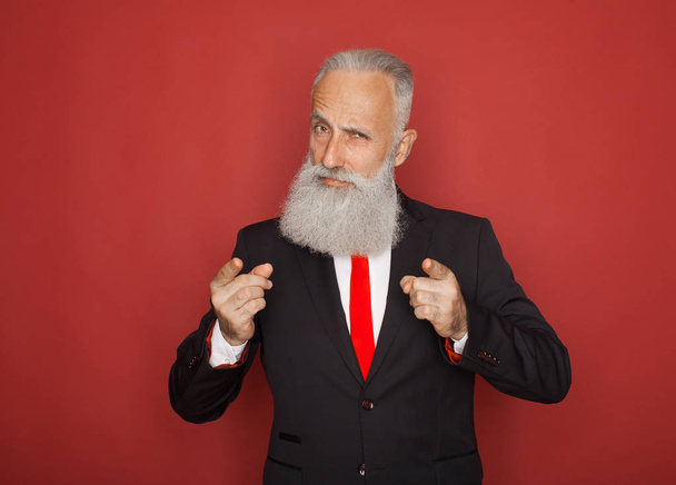 Portrait of a confident senior businessman pointing finger at camera isolated over red background - Foto, imagen