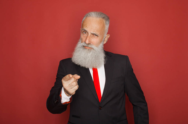 Portrait of a confident senior businessman pointing finger at camera isolated over red background - Fotó, kép