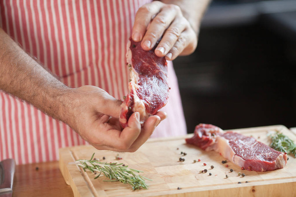 Hands of a man preparing meat and vegetables in a kitchen slicing lean meat on a wooden board. - Foto, Bild