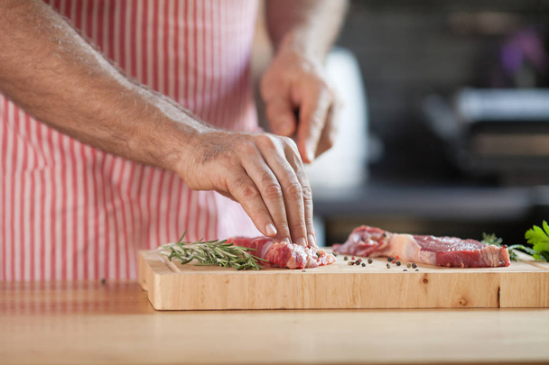 Hands of a man preparing meat and vegetables in a kitchen slicing lean meat on a wooden board. - Foto, Imagem