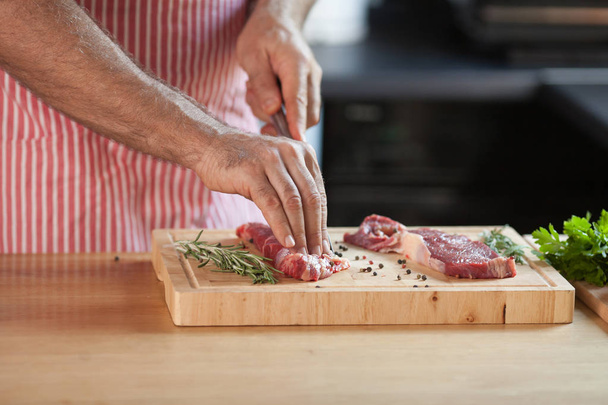 Hands of a man preparing meat and vegetables in a kitchen slicing lean meat on a wooden board. - Fotoğraf, Görsel
