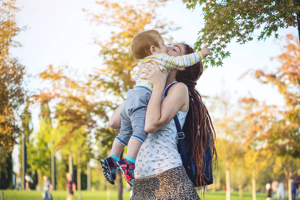 Jovem mãe feliz moderna com bebê filho andando em Sunny Park. O conceito da alegria da maternidade e do clima de outono
 - Foto, Imagem