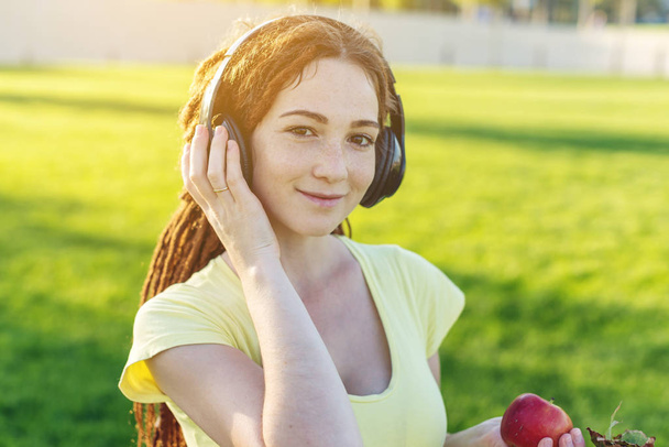 Mooie moderne vrouw luisteren naar muziek met haar koptelefoon op de achtergrond van de natuur in het najaar van Sunny Park. Het concept van goed humeur, favoriete muziek, gelukkige tijd. - Foto, afbeelding