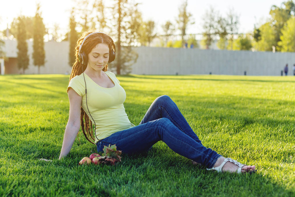 Piękna nowoczesna kobieta słuchanie muzyki z jej słuchawki na tle przyrody jesienią słoneczny Park. Pojęcie dobrego nastroju, ulubionej muzyki, szczęśliwy czas. - Zdjęcie, obraz