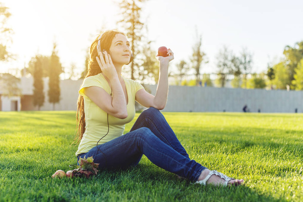 Mooie moderne vrouw luisteren naar muziek met haar koptelefoon op de achtergrond van de natuur in het najaar van Sunny Park. Het concept van goed humeur, favoriete muziek, gelukkige tijd. - Foto, afbeelding
