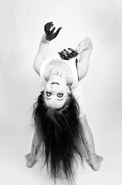 Halloween. Portret gebogen over de rug van een zombie meisje met zwarte aders op haar gezicht. concept van halloween en Allerzielen. - Foto, afbeelding