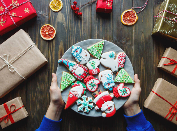 Дети руки с тарелкой полный ручной работы пряничного хлеба: Санта, снежинка, олень, ель, снеговик формы на темном деревянном фоне с подарками. Концепция украшения Рождества и Нового года
 - Фото, изображение