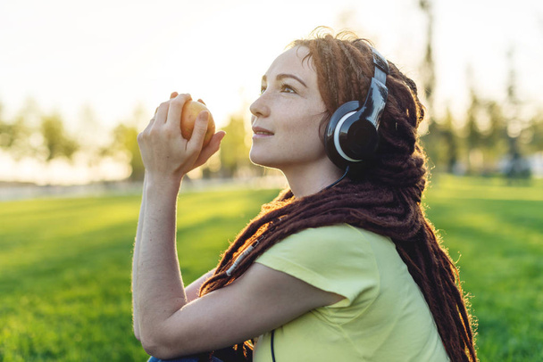 Mulher moderna bonita ouvir música com seus fones de ouvido no fundo da natureza no outono Sunny Park. O conceito de Melomania e bom humor
 - Foto, Imagem