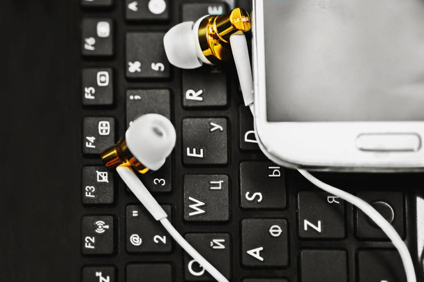 Black keyboard of laptop with white mobile phone and headphone  - Photo, Image