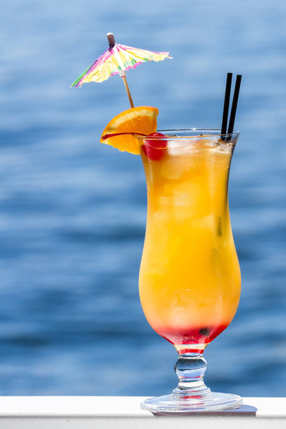 tropical cocktail served outside with a natural blue water background as a travel holiday concept - Photo, Image