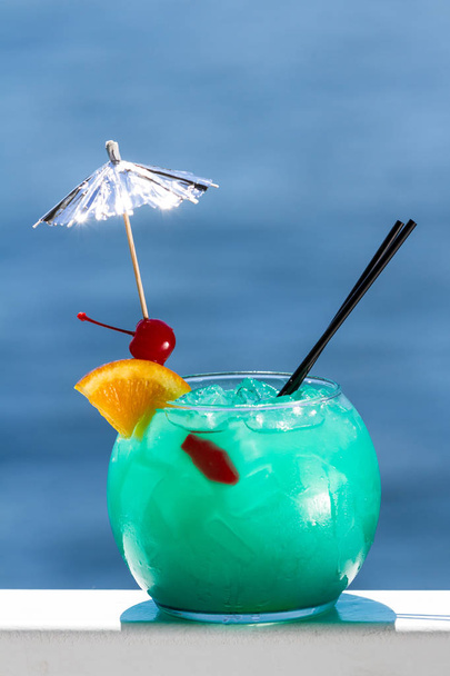 blauer Cocktail in einer Fischschale, serviert auf einem Geländer mit natürlichem Wasserhintergrund als Reisekonzept - Foto, Bild