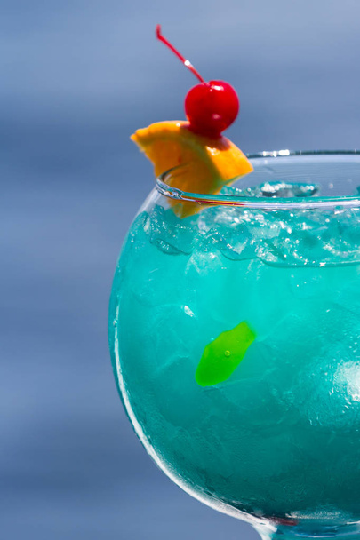 blauwe cocktail geserveerd in een vis kom geserveerd op een trapleuning met een natuurlijke water achtergrond als reizen concept - Foto, afbeelding
