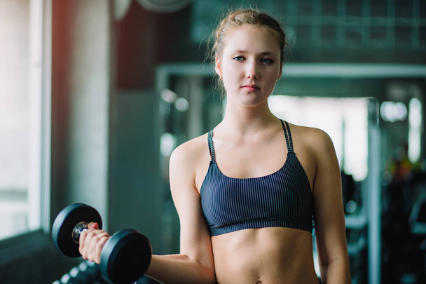 Fit beautiful young woman caucasian posing at the camera in sportswear. Young woman holding dumbbell during an exercise class in a gym. Healthy sports lifestyle, Fitness concept. With copy space. - Foto, Imagem