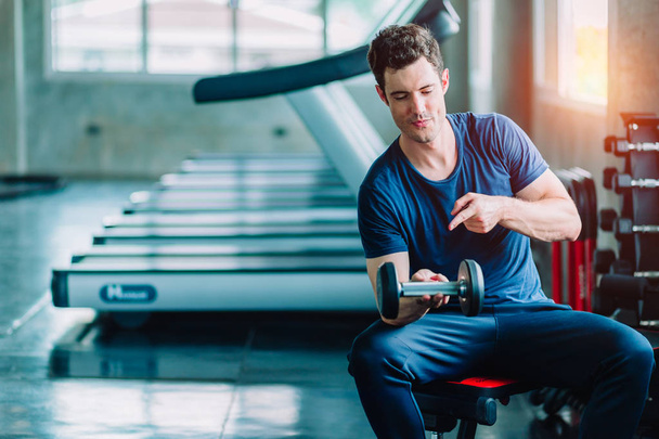 Fit caucasian handsome young man and big muscle in sportswear. Young man holding dumbbell during an exercise class in a gym. Healthy sports lifestyle, Fitness concept. with copy space for your text. - 写真・画像
