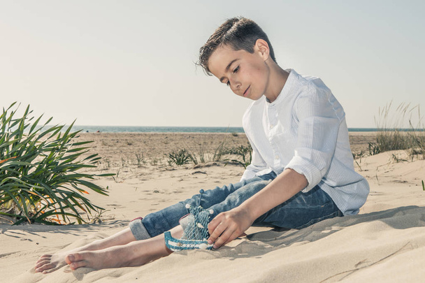 boy sitting on the beach sand in a white dress - Photo, Image