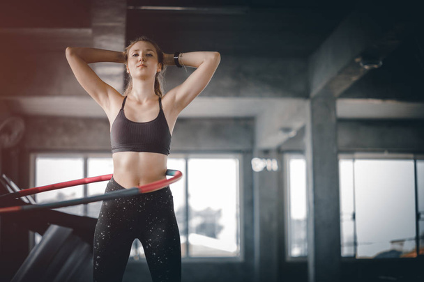 Beautiful caucasian young woman doing hula hoop in step waist hooping forward stance. Young woman doing hula hoop during an exercise class in a gym. Healthy sports lifestyle, Fitness, Healthy concept. - Photo, Image
