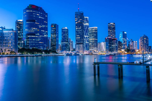 Vista lateral de la persona tendida en el muelle y mirando rascacielos iluminados en la orilla del río por la noche en Brisbane, Australia
 - Foto, Imagen