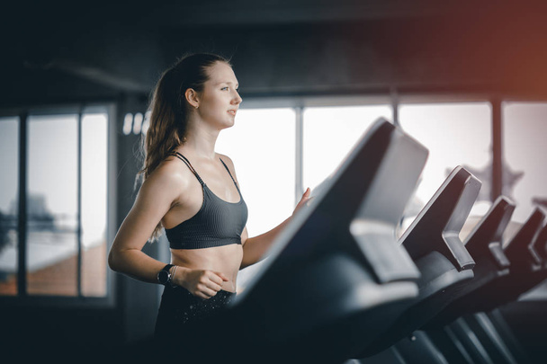 Fit young woman caucasian running on machine treadmill workout in gym. Glad smiling girl is enjoy with her training process. Concept of fitness, healthy life, Sport, Lifestyle. - Foto, imagen